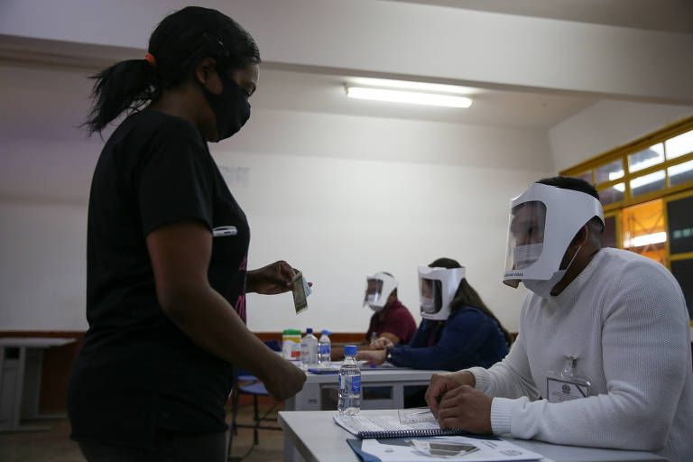 Com máscaras e aparatos de proteção facial, mesários coordenam a votação em Valparaíso, Goiás, em 2020,  em meio à pandemia da Covid-19. 