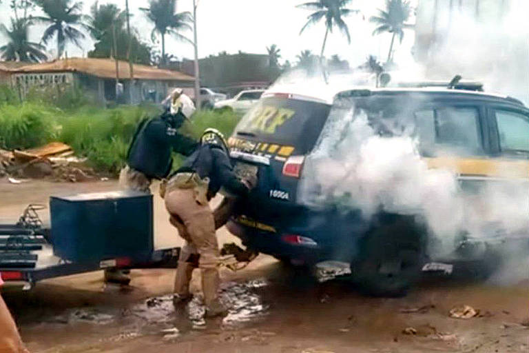 dois policiais de capacete colocam homem em porta-mala de viatura da PRF