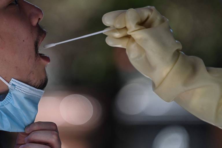Imagem mostra homem de boca aberta enquanto profissional de saúde coloca cotonete para teste.