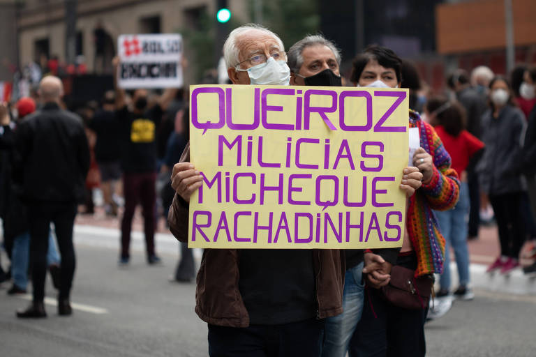 Manifestante com cartaz onde se lê "Queiroz, milícias, micheque e rachadinhas"