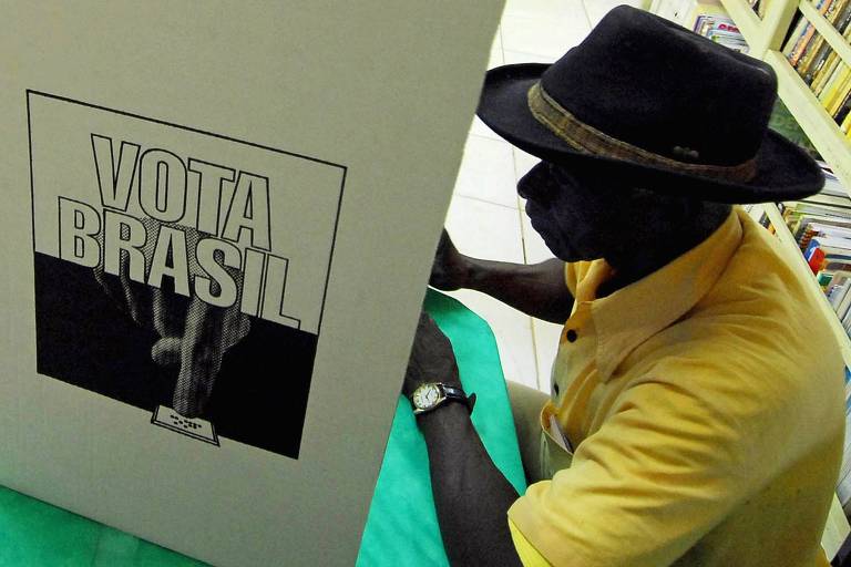 Homem negro vestido com camisa amarela e chapéu aparece de perfil; à sua frente está a cabine de votação, onde se lê "vota Brasil"