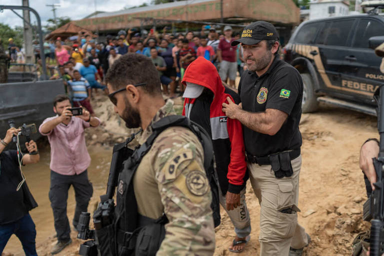 Policiais federais levam Pelado, suspeito de assassinar Dom Phillips e Bruno Pereira, observados por moradores de Atalaia do Norte