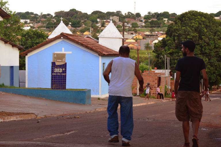 Dois homens negros caminhando por rua com igreja azul ao fundo