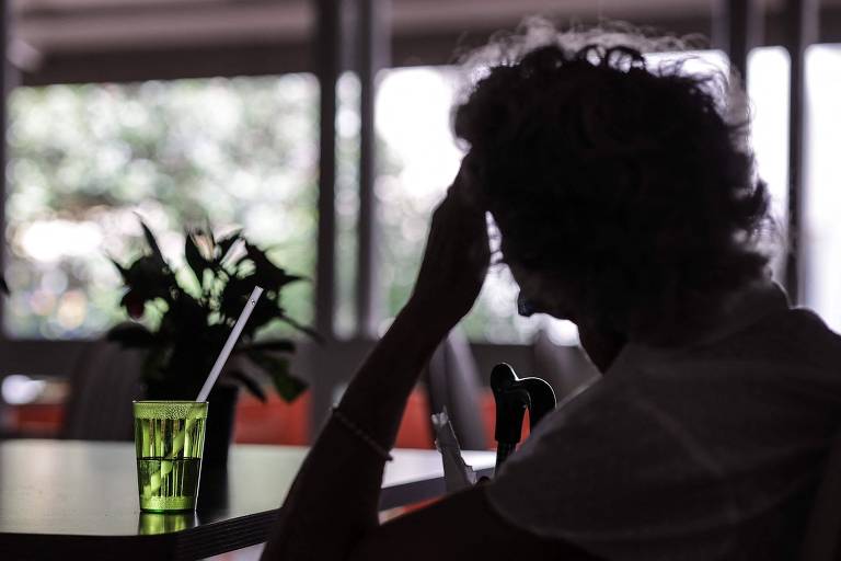 Mulher vista de costas com um copo de bebida com um canudo dentro apoiado em uma mesa