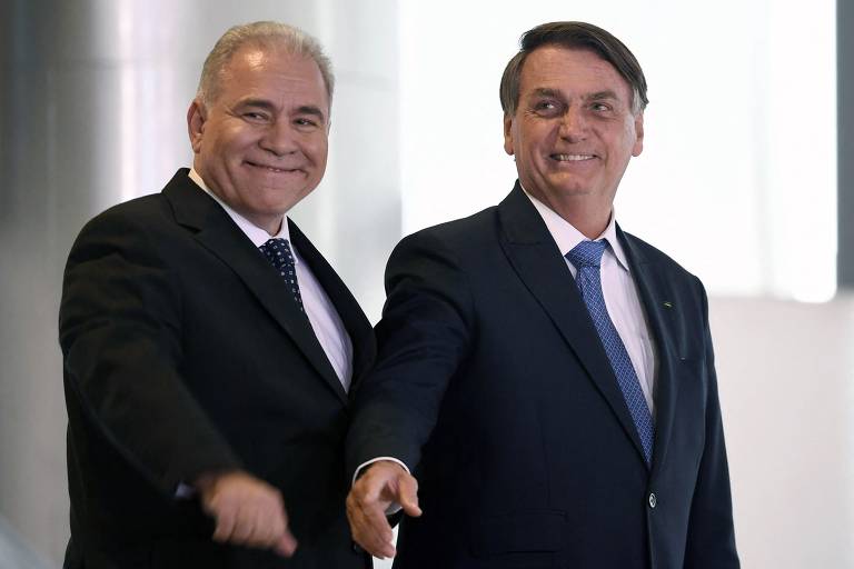 O presidente Jair Bolsonaro e o ministro da Saúde, Marcelo Queiroga, durante evento no Palácio do Planalto. Os dois aparecem lado a lado, vestindo ternos escuros e sorrindo, em momento de descontração