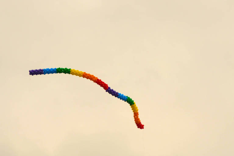 Uma fileira de balões multicoloridos sobrevoa o céu, que aparece meio amarelado. Também se vê uma antena de transmissão do lado direito da imagem