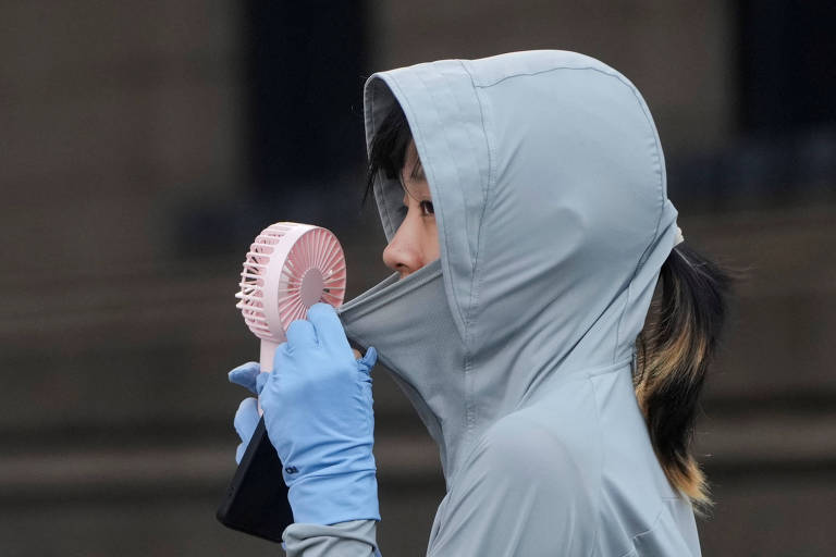 Mulher com roupa que protege contra o sol usa ventilador em rua de Xangai, na China