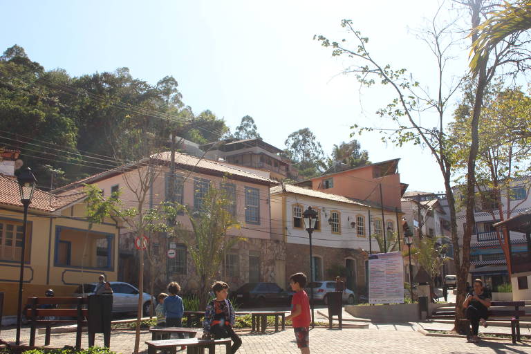 registro da praça central da cidade, onde crianças estão sentadas. em segundo plano, estão algumas casas