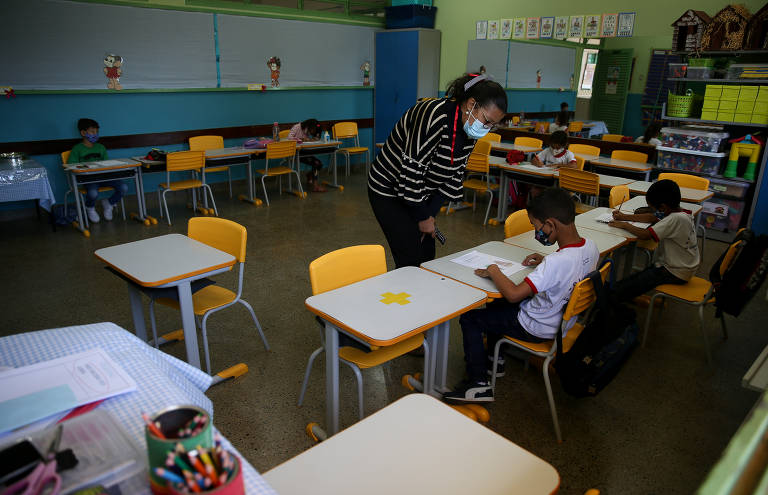 Professora de máscara orienta aluno sentado em carteira