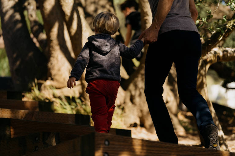 Homem caminha segurando a mão de seu filho