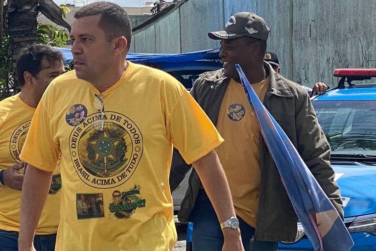 O ex-segurança e ex-assessor de Jair Bolsonaro, Max de Moura, aparece em ato de campanha, ao lado de outras pessoas. No fundo, há viaturas da Polícia Militar do Rio de Janeiro.