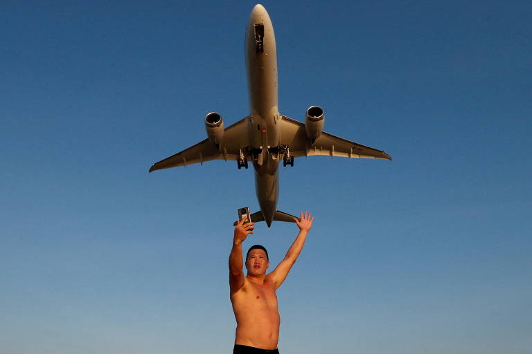 Turista faz selfie em praia próxima do aeroporto internacional de Phuket, na Tailândia, enquanto avião decola