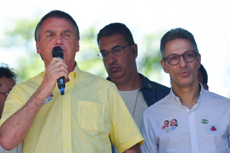 O presidente Jair Bolsonaro, de camisa amarela, discursa no microfone com o governador de Minas Gerais, Romeu Zema, de camisa branca, do seu lado esquerdo