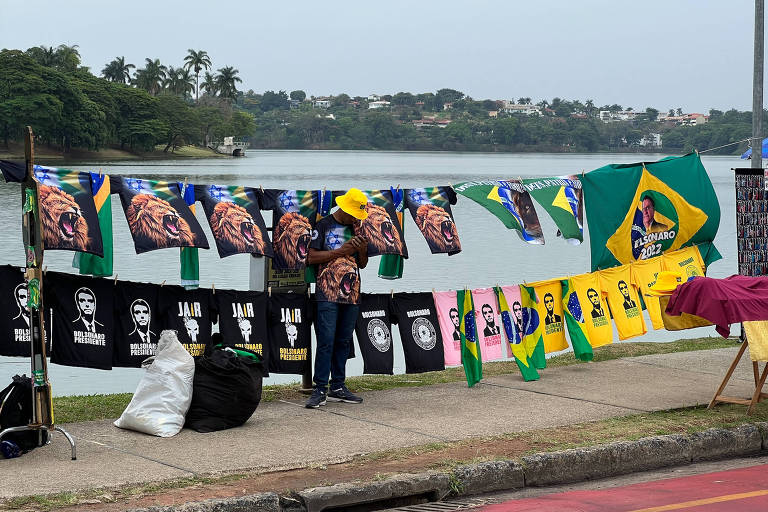 Camisas e bandeiras com a estampa de Bolsonaro penduradas em varais; ao fundo, a Lagoa da Pampulha