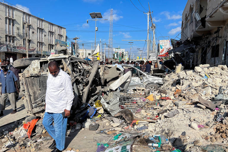 Homem de calça jeans e camisa branca caminha por escombros de edifícios e carros destruídos depois de atentado na Somália 
