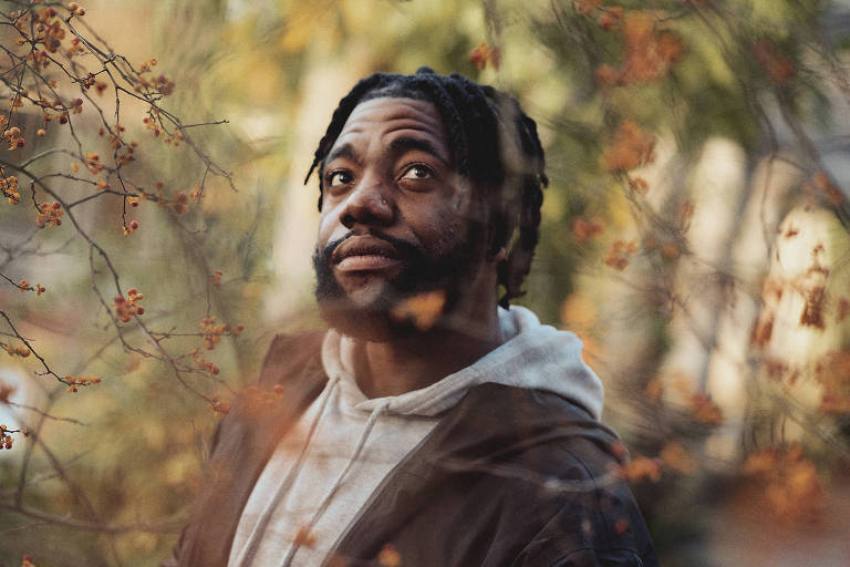 Retrato de homem negro em meio a galhos com folhas amareladas pelo outono