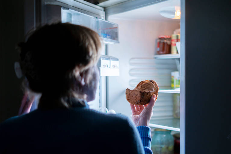 Mulher comendo bolo à noite na geladeira