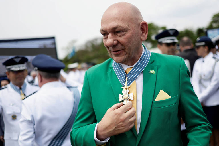 Luciano Hang é um homem branco e calvo que usa um terno verde e amarelo.