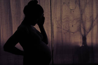 Silhouette of a woman holding her head during pregnancy. Pregnant woman in sadness at the window