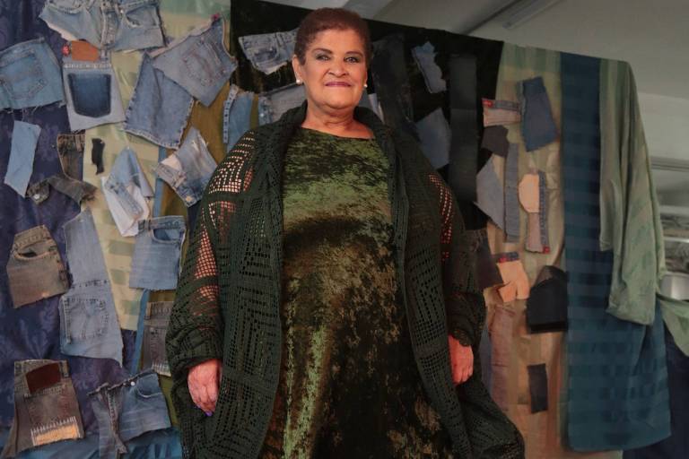 mulher de 60 anos com roupas verdes e sandália preta em frente a um painel grafitado