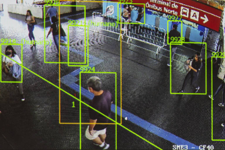 Imagem em câmera mostra quadrados verdes e amarelos em volta de pessoas que passam por uma estação de metrô