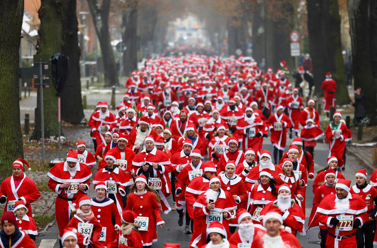 Em uma via com arvores grandes, centenas de pessoas vestidas de Papai Noel correm em direção à fotógrafa.