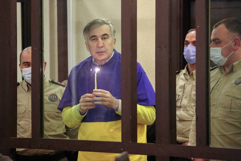 O ex-presidente da Geórgia Mikheil Saakashvili segura vela enquanto reza pela Ucrânia no banco dos réus, durante audiência em Tbilisi