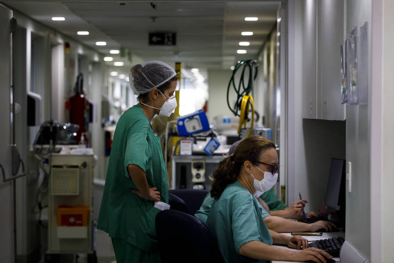 Imagem mostra enfermeiras em um corredor de hospital. Algumas delas estão sentadas e outras, em pé.