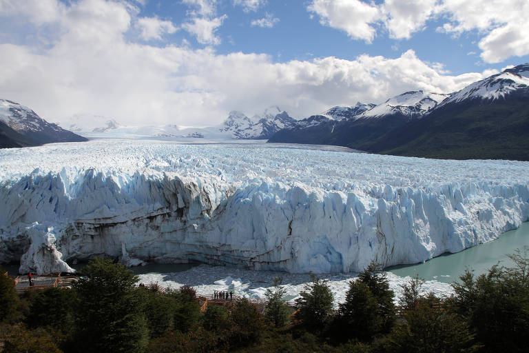 Vista do glaciar enorme com montanhas ao lado sob um céu azul com nuvens brancas