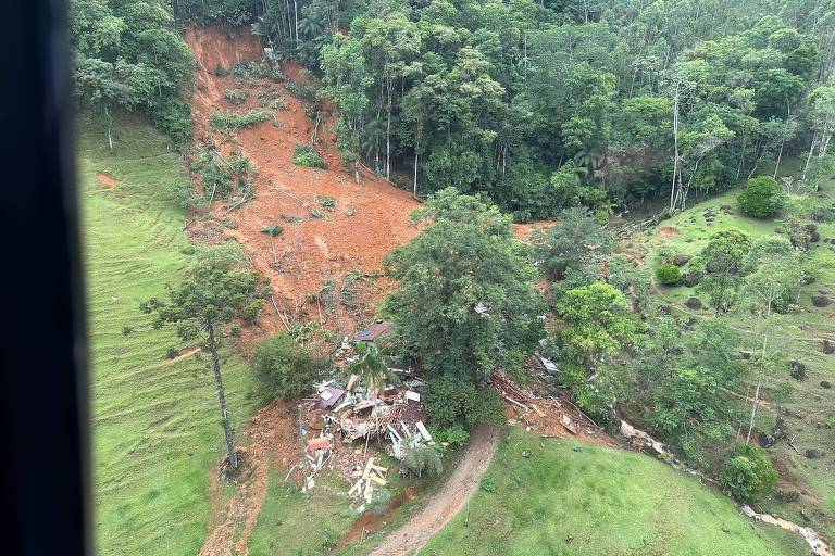 Foto colorida mostra destroços de várias casas destruídas abaixo de um grande deslizamento de terra entre a mata do Morro do Pico, no Vale do Itajaí, após fortes chuvas em Santa Catarina