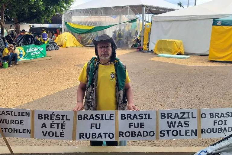 Candidato derrotado a deputado estadual, o jornalista Adrian Paz (PRTB-MG) foi preso em Brasília após atos golpistas de 8 de janeiro. Na imagem ele aparece em acampamento em frente ao quartel-general do Exército, em Brasília, com cartazes afirmando que o Brasil foi roubado