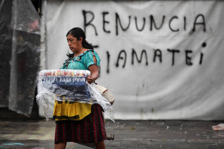 Vendedora caminha em rua da Cidade da Guatemala perto de faixa que pede a renúncia do presidente Alejandro Giammattei 