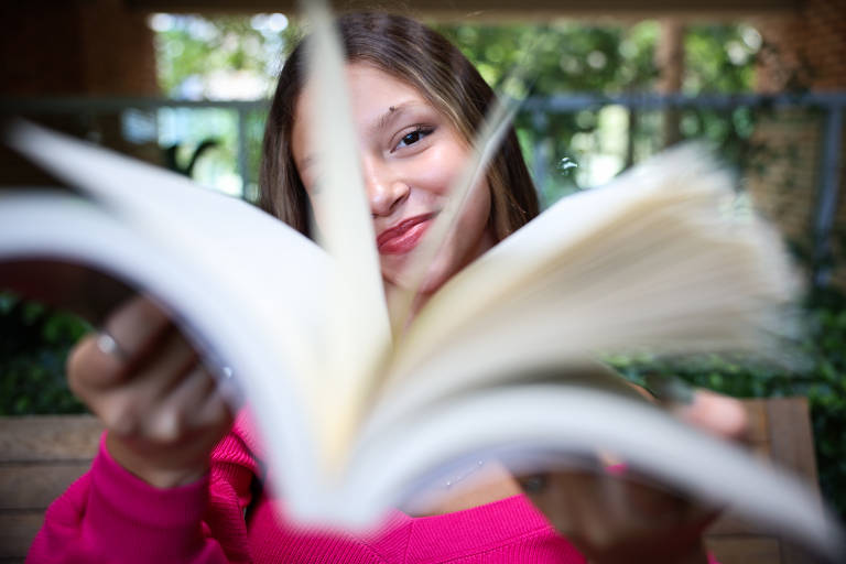 Jovem sorri para a câmera enquanto estende um livro