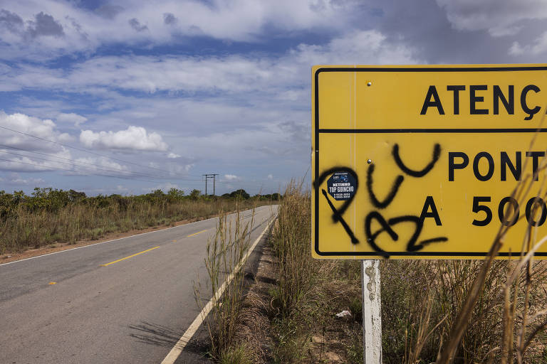 Placa de sinalização de trânsito, amarela, pichada com "PCC", em alusão à facção criminosa