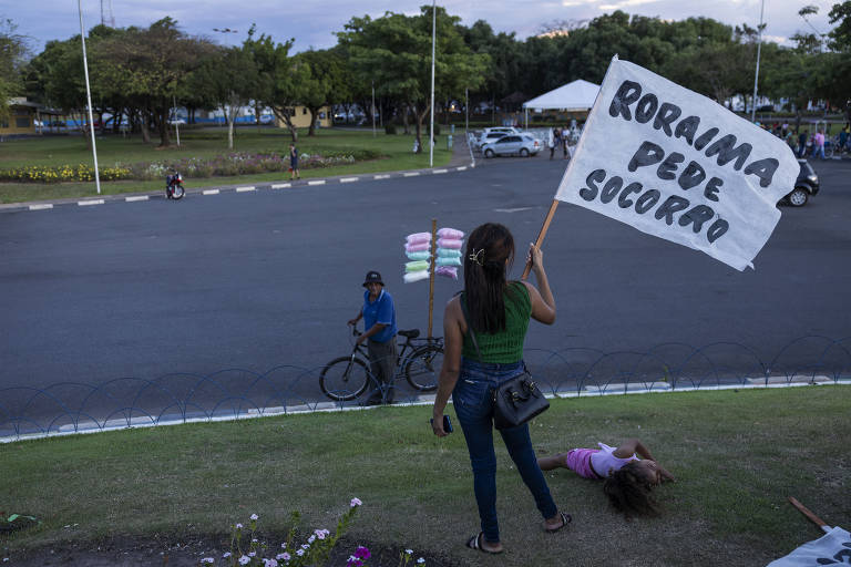 Mulher, de costas, segura faixa com a frase 'Roraima pede socorro'