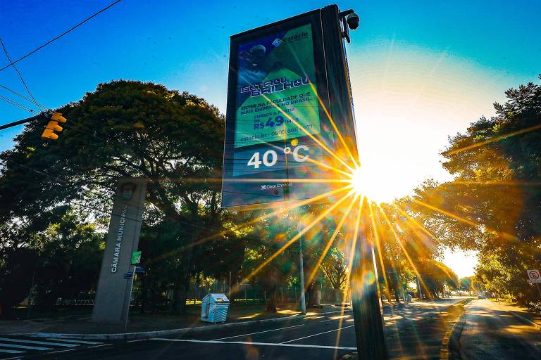 Relógio marcando 40 graus com o sol iluminando copas de árvores.