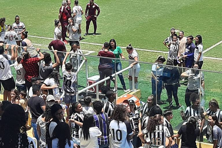 jogadoras de futebol se abraçam perto de alambrado da torcida