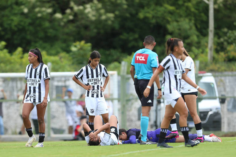 jogadoras deitadas choram observadas por colegas em campo
