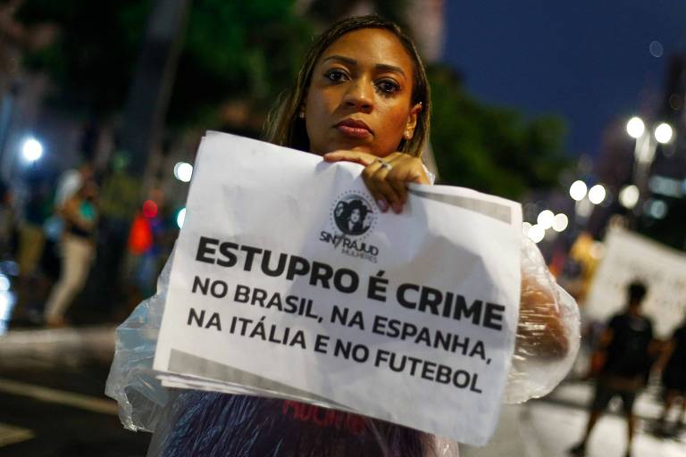 Mulher mostra cartaz que diz: Estupro é crime - No Brasil, na Espanha, na Itália e no futebol