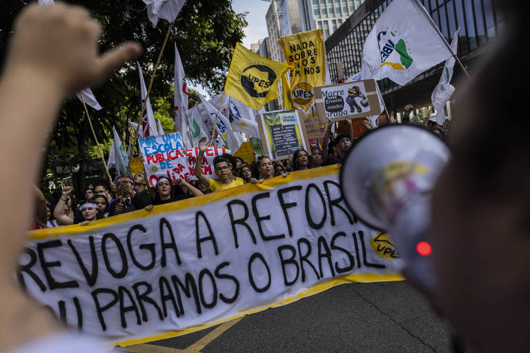 Estudantes carregam faixa pedindo revogação da reforma do ensino médio: "Ou revoga a reforma ou paramos o Brasil"; na frente deles, um jovem fala em megafone