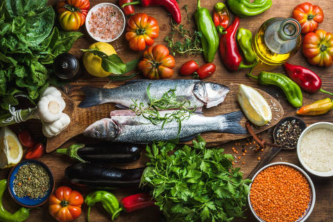 Raw uncooked seabass fish with vegetables, grains, herbs and spices on chopping board over rustic wooden background. Credito Sonyakamoz / Adobe Stock