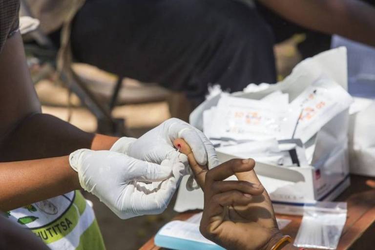 Enfermeiro fura o dedo de uma pessoa para fazer exame de sangue