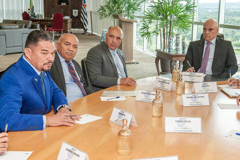 Alexandre de Moraes com os deputados distritais Hermeto, Chico Vigilante e Wellington Luiz. Os quatro estão sentados em uma mesa de madeira no gabinete do ministro. Moraes está à direita dos demais