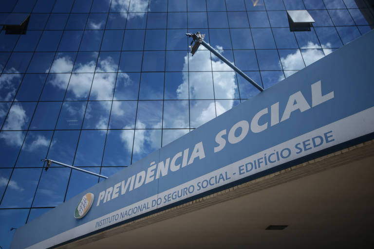 A imagem mostra a fachada do edifício-sede do Instituto Nacional do Seguro Social, da Previdência Social, com o céu azul e nuvens refletidos nas janelas de vidro do prédio