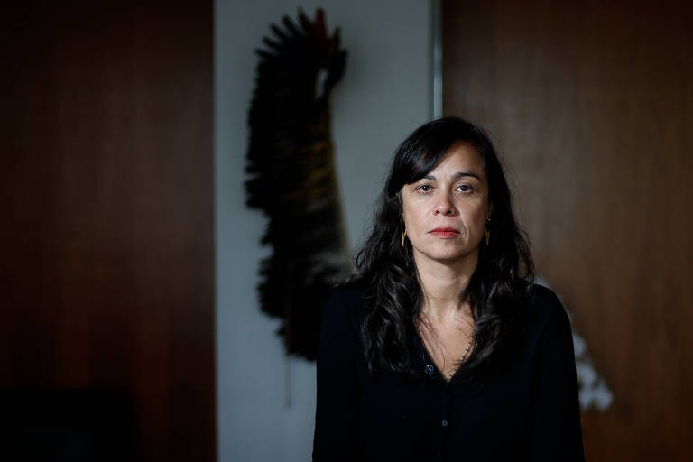 Mulher com cabelos longos e roupa preta posa ao lado de um cocar no Ministério dos Povos Indígenas
