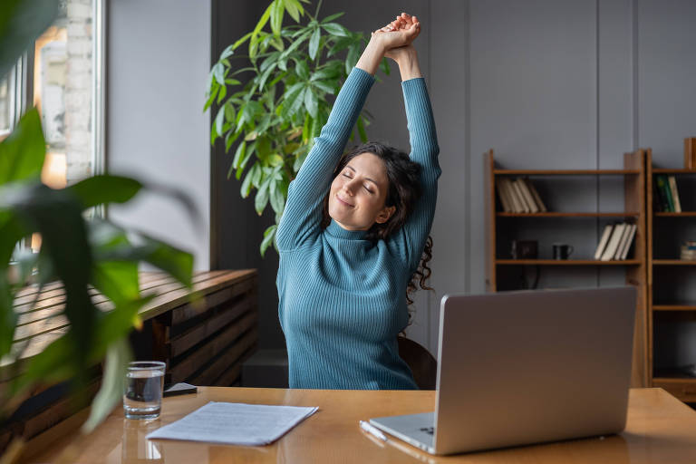 Mulher de negócios feliz aquecendo o corpo e os músculos no local de trabalho, sentindo-se satisfeita com o trabalho realizado, funcionária sorridente descansando da tela do computador. Bem-estar, produtividade e felicidade no trabalho