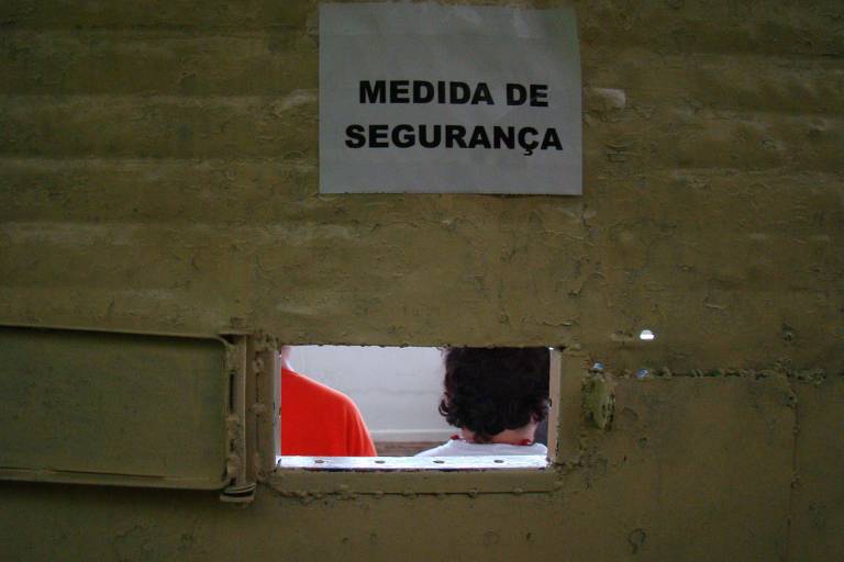 foto mostra porta com pequena abertura no meio, onde é possível ver o cabelo de uma pessoa que está de costas