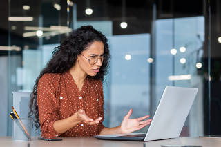 Frustrated business woman looking at laptop screen, dissatisfied female worker spreading hands inside office, latin american woman working at desk using computer for video call online communication