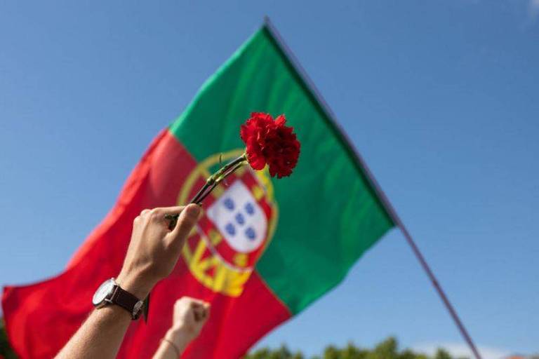 mão ergue cravo diante de bandeira de portugal