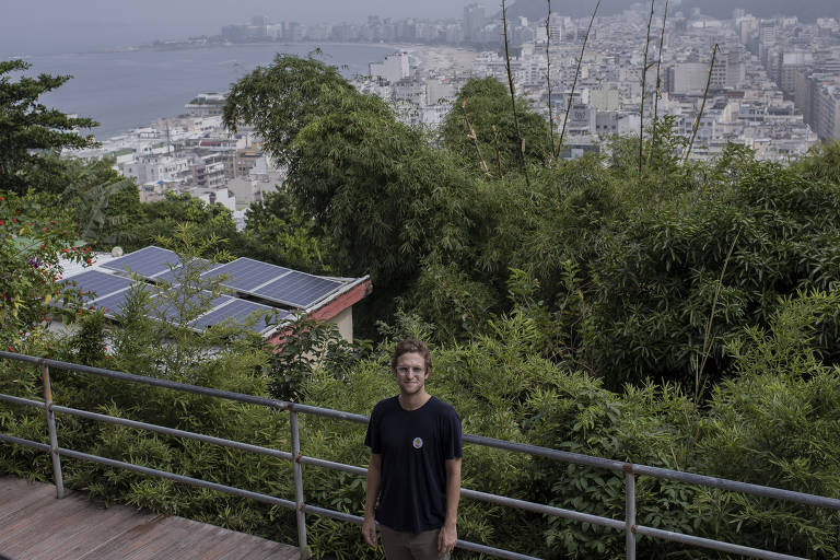 Imagem colorida mostra retrato, em plano aberto, do economista Eduardo Avila fundador da ONG Revolusolar. Ao fundo, é possível ver placas de energia solar instaladas em casas da comunidade.